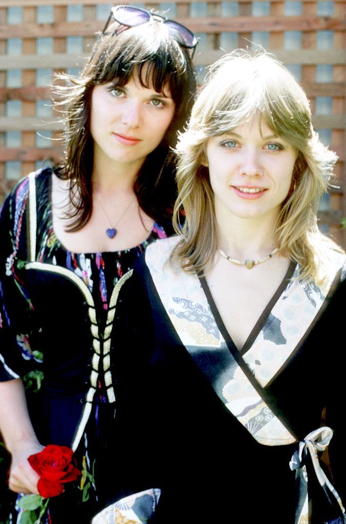 two women standing next to each other in front of a brick wall and one is holding a rose