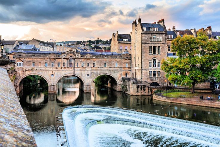 a river running through a city next to tall buildings and a bridge with a waterfall coming out of it