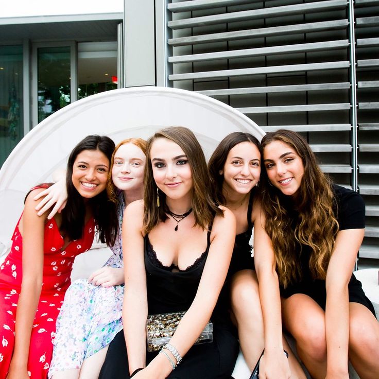 four women sitting on a bench in front of a building