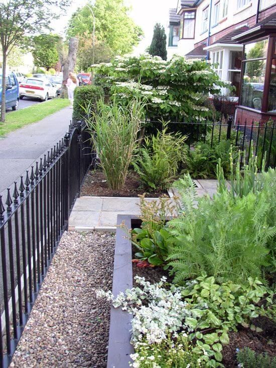 a black fence is next to some plants and flowers on the side of the road