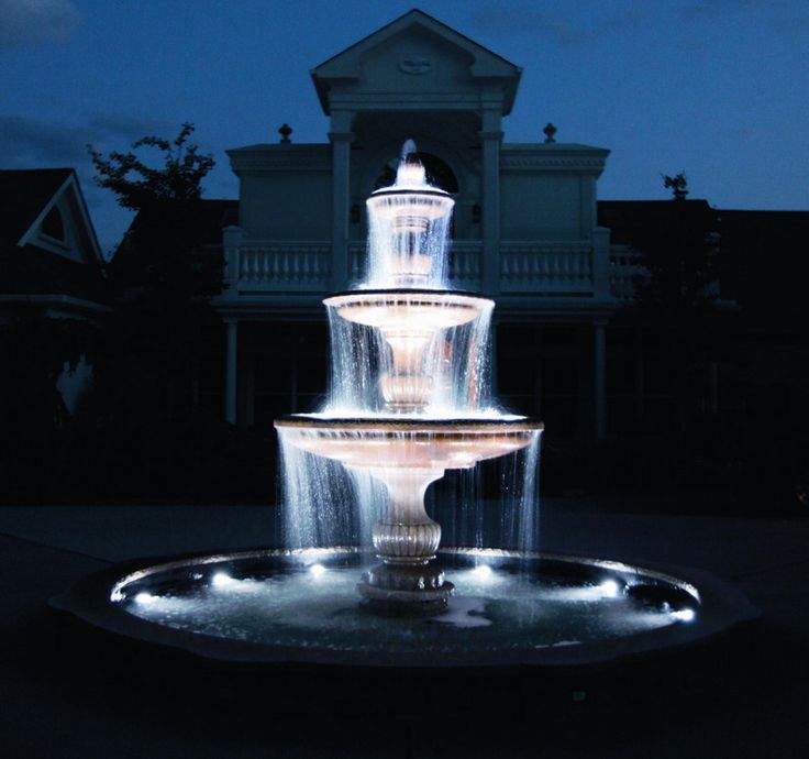 a lighted fountain in front of a house at night