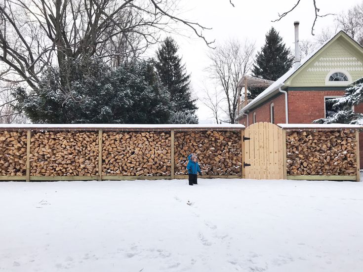 a person standing in the snow next to a fence made out of logs and wood