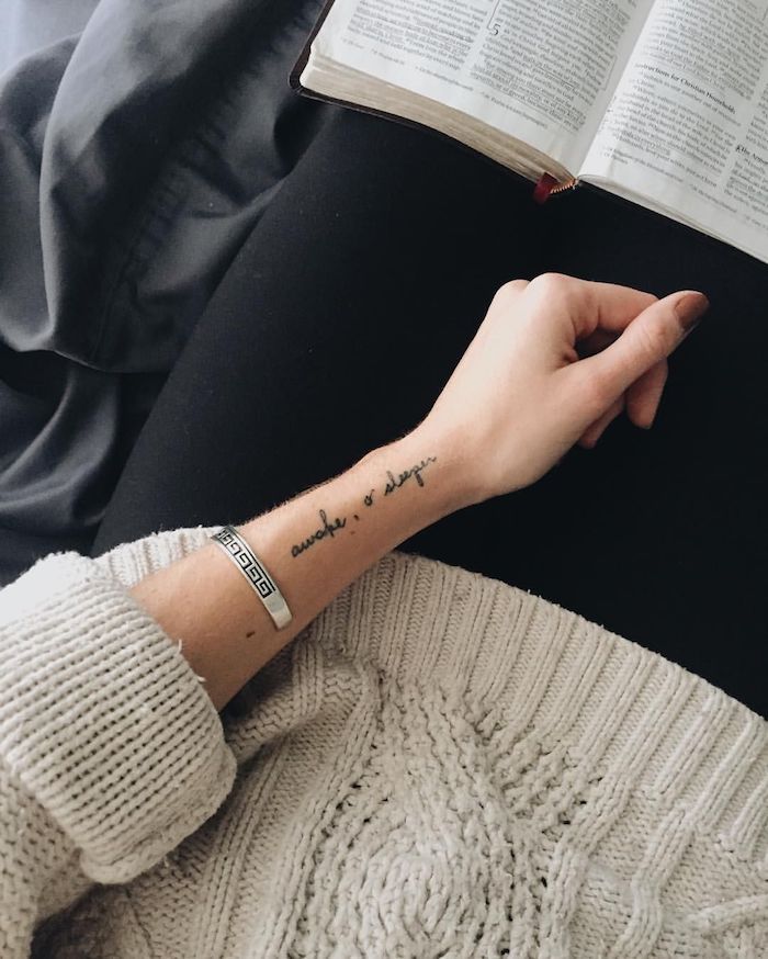 a person with a book in their hand and a tattoo on their arm reading a book