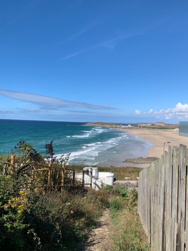 the beach is next to an old wooden fence and some bushes on the side of the road