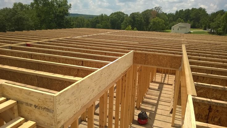 an unfinished house being built with wood framing on the floor and roof, surrounded by trees