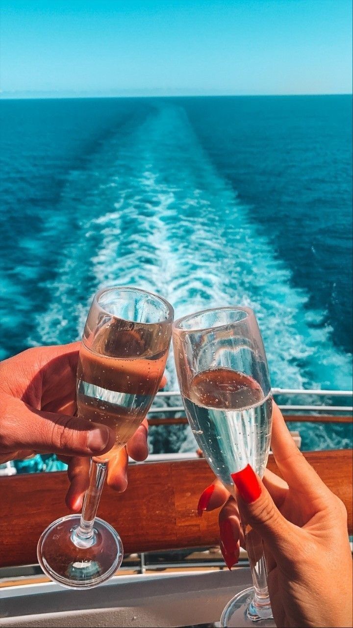 two people toasting with wine glasses on a boat in front of the ocean and blue sky