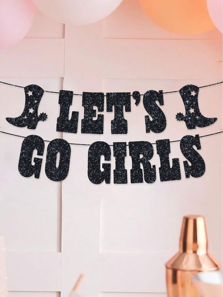 there is a sign that says let's go girls hanging from a string with balloons in the background