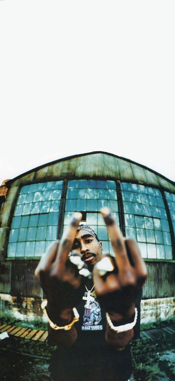 a man standing in front of a building making the v sign with his hands while wearing a hat