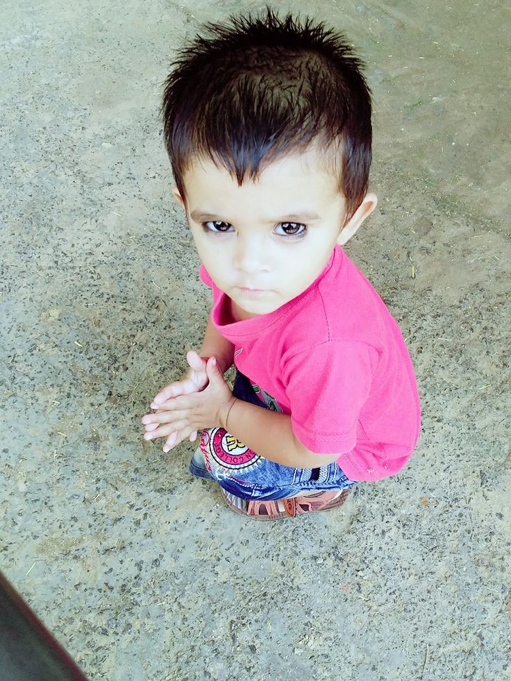 a little boy sitting on the ground with his hands in his pockets and looking at the camera