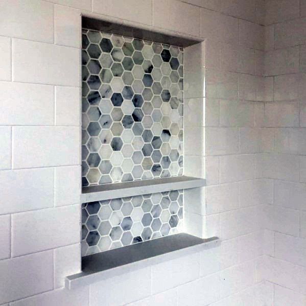 a white bathroom with hexagonal tiles on the shower wall and shelves in the corner