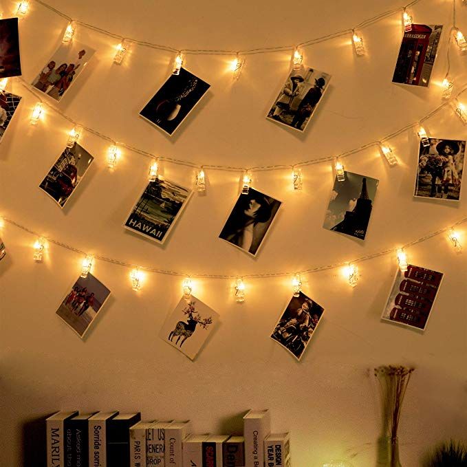 there is a string of lights strung over the bookshelf with pictures on it