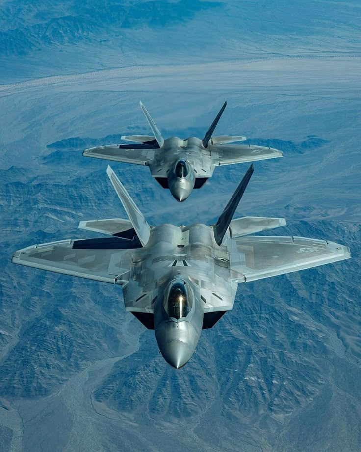 two fighter jets flying side by side in the sky over mountains and desert terrains