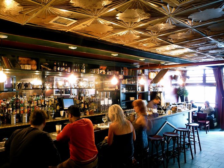 several people sitting at a bar with their backs turned to the camera and one person standing in front of the bar