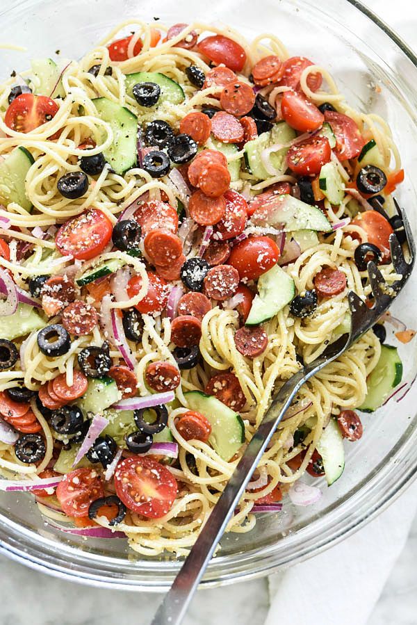 a glass bowl filled with pasta salad topped with cucumbers, tomatoes and olives