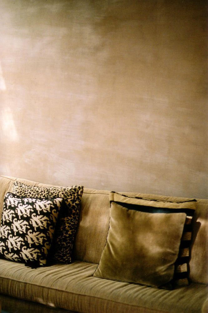 a couch with several pillows on it in front of a wall that has been painted gold