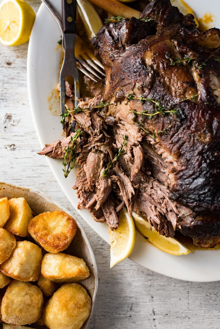 roast beef with potatoes and lemons on a white plate next to a knife and fork