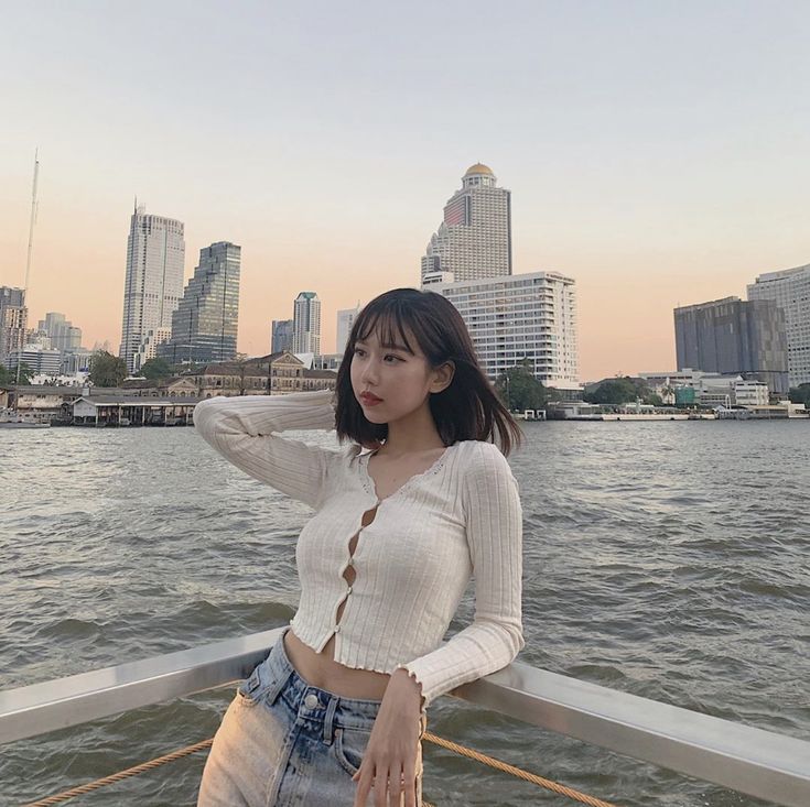 a woman standing on top of a boat in the water next to a large city