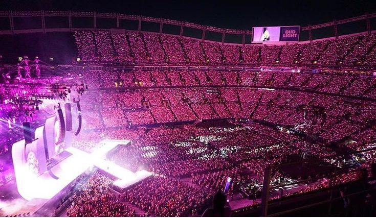 a large stadium filled with lots of people and purple lighting on the side of it