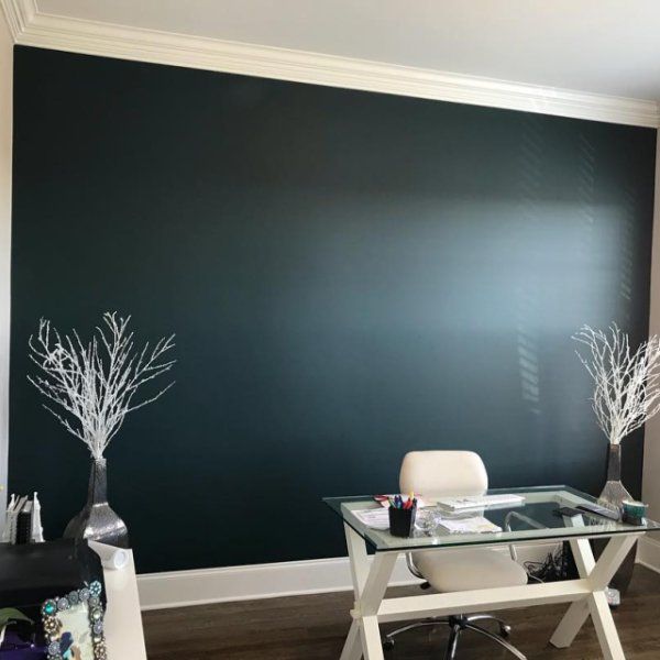 an office with a glass desk and white chairs in front of a wall painted black