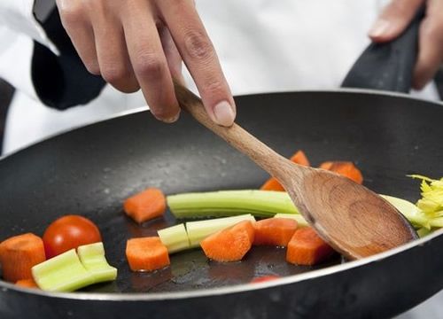 a person cooking vegetables in a wok with a wooden spoon