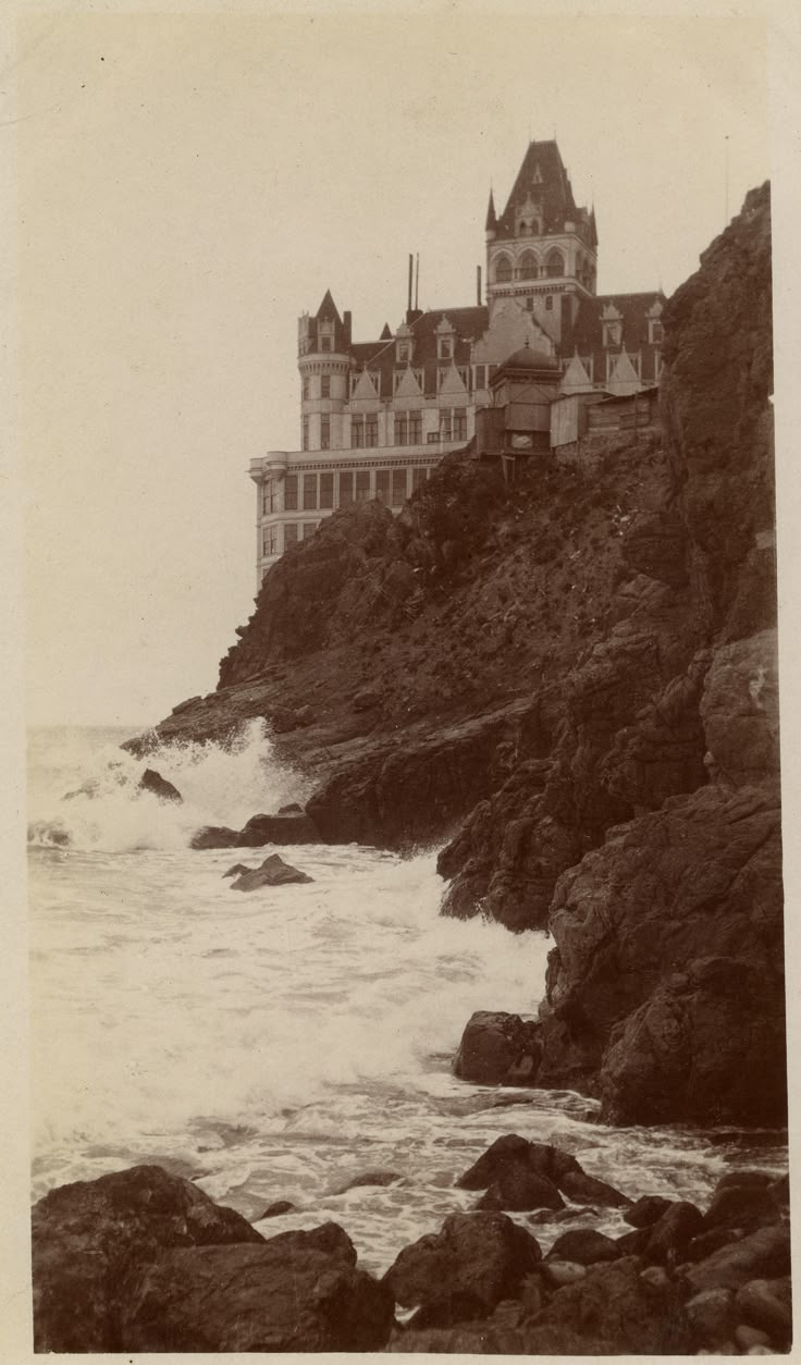 an old black and white photo of a castle by the ocean with waves coming in