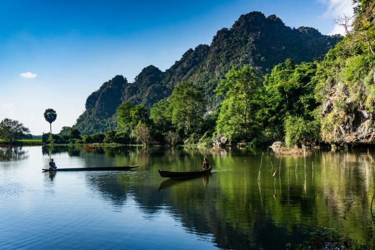 a man in a boat on a river surrounded by green mountains and trees with blue sky