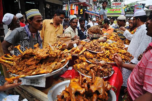 many people are standing around a table full of food and looking at the food on it