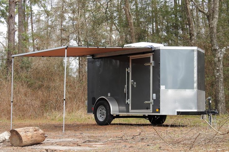 an enclosed trailer parked in the middle of a wooded area with a canopy over it