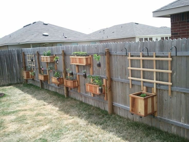 a wooden fence with several planters on it and some grass in the back yard