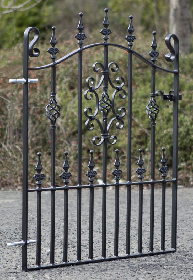 an iron gate is shown in the middle of a gravel area with trees and bushes behind it