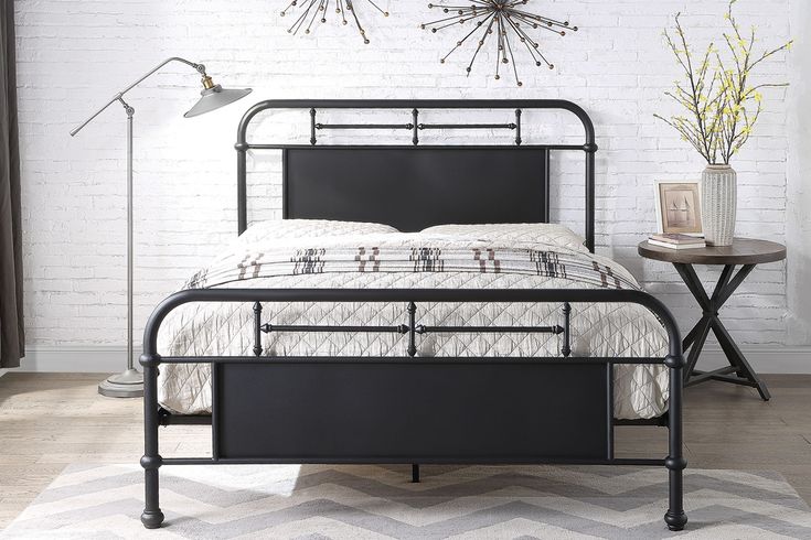 a black metal bed frame with white sheets and pillows on top of it next to a side table