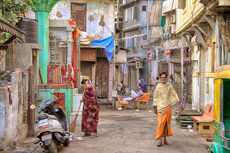 two people are walking through an alleyway in the middle of some buildings with colorful doors and windows