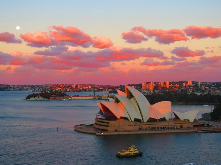 the sydney opera house is lit up in pink and blue as the sun sets over the city