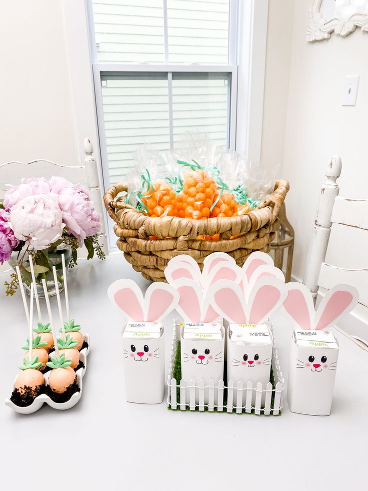 a table topped with cupcakes and bunny ears on top of each other next to a basket filled with carrots