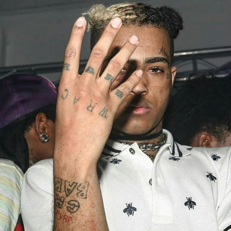 a man with tattoos holding his hand up to his face while sitting in front of other people