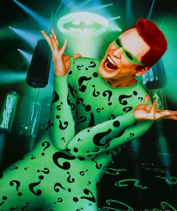 a man dressed in green and black with question marks all over his body, posing for the camera