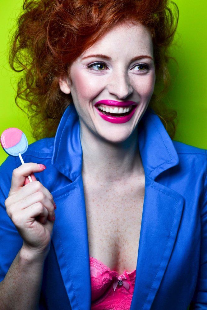 a woman with red hair holding a lollipop in her right hand and smiling