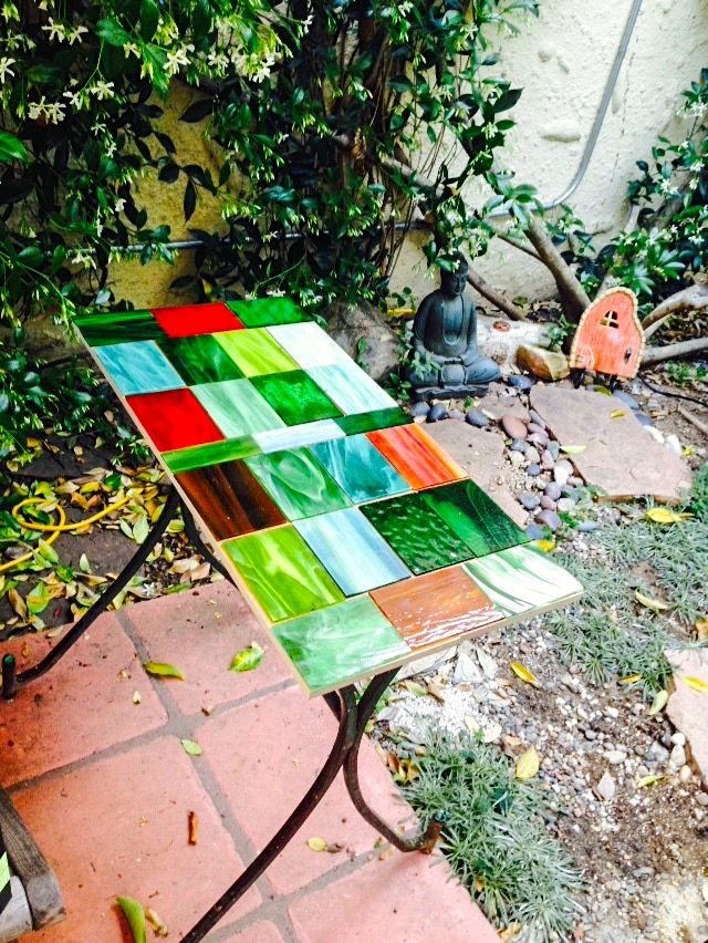 a multicolored glass table sitting on top of a brick sidewalk next to a tree