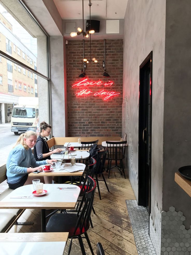 people sitting at tables in a restaurant with neon signs on the wall and windows behind them