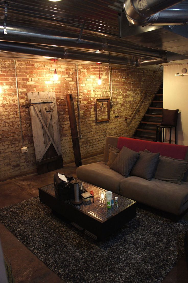 a living room filled with furniture and exposed pipes on the wall above it's stairs