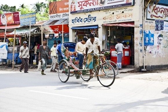 people are walking and riding bicycles in front of shops on a street with parked cars