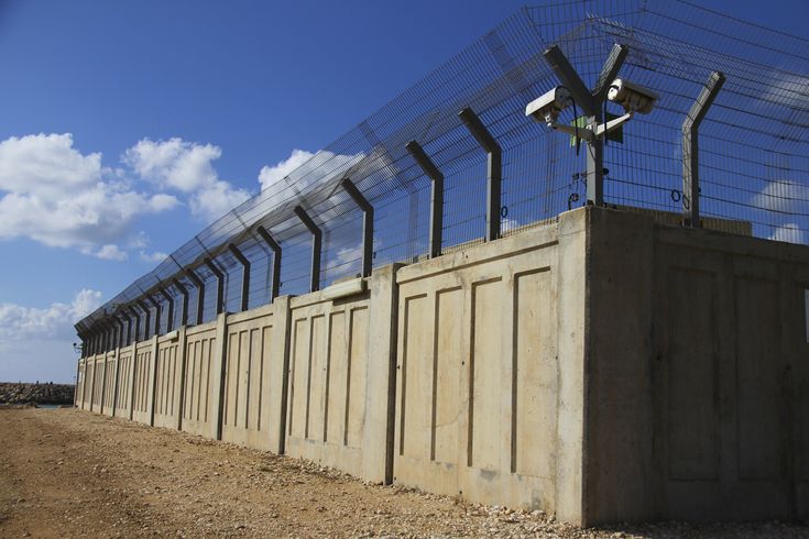 a row of fenced in cell phones sitting on top of a dirt field next to a blue sky