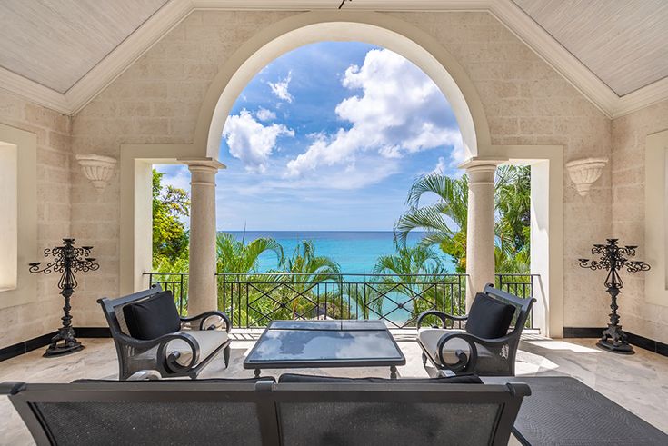 an outdoor living area with chairs and tables overlooking the ocean in front of a large arched window