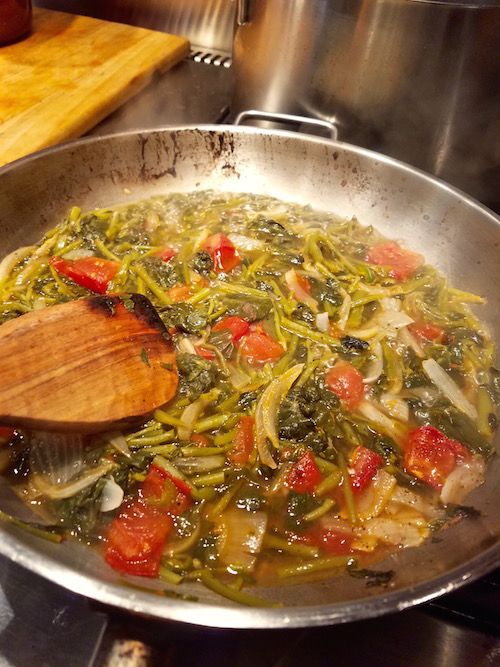 a wok filled with vegetables on top of a stove next to a wooden spoon