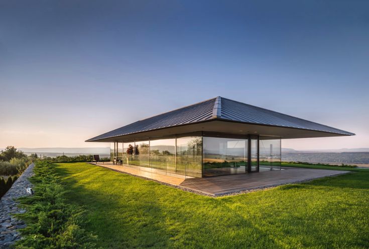 the glass pavilion sits on top of a grassy hill