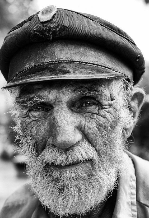 an old man wearing a hat and smiling for the camera with trees in the background