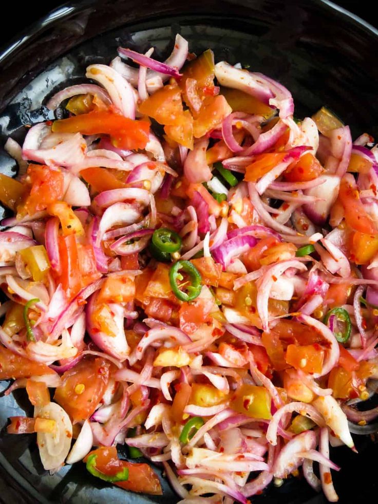 a black bowl filled with red onions and green peppers