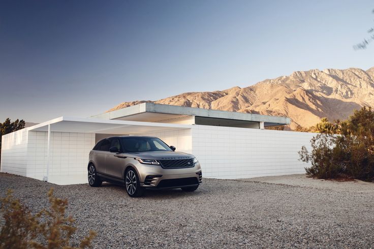 a silver range rover parked in front of a white house with mountains in the background