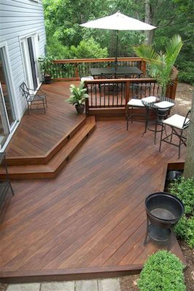 a wooden deck with chairs and an umbrella on the top floor next to a tree