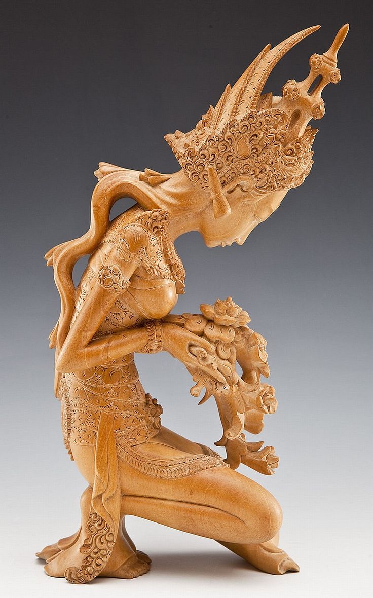 a carved wooden figure holding a vase in its hands and looking down at it's body